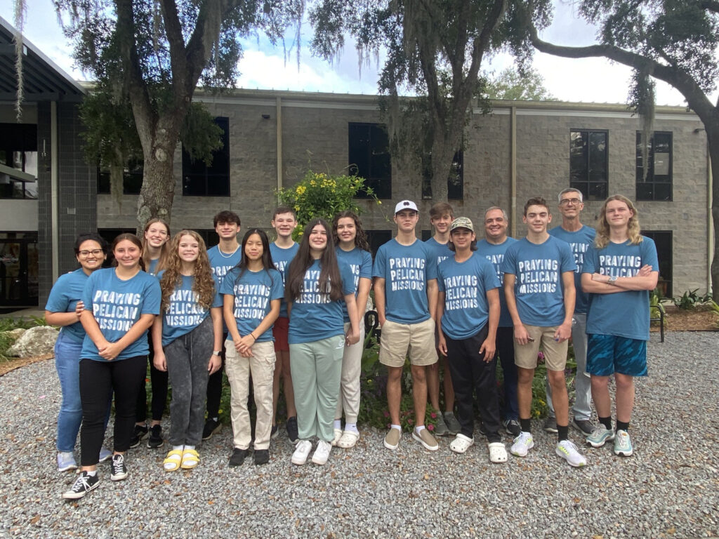 A group of High School students wearing matching t-shirts that read, "Praying, Pelican, Missions."