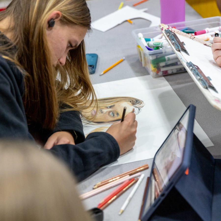 A high school student focuses intently on her artwork whilst adding color with colored pencils.