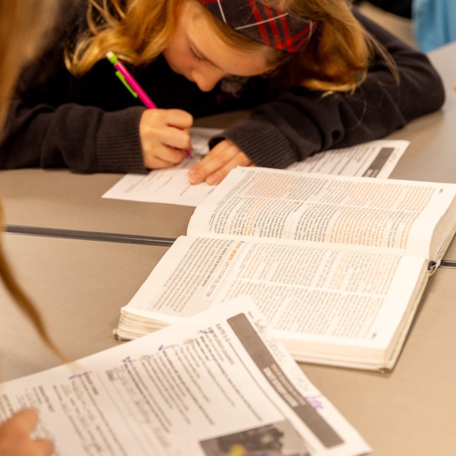 Elementary school girl hunched over worksheet with Bible open beside her on the desk.