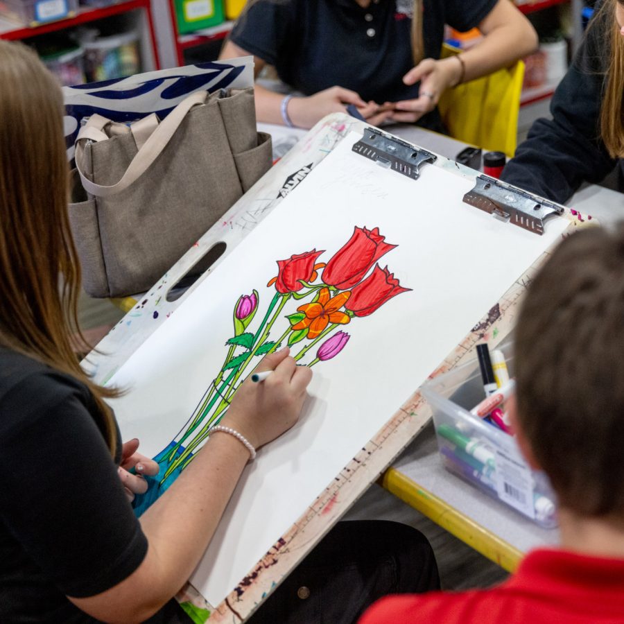 A student drawing a bouquet of flowers on with markers.