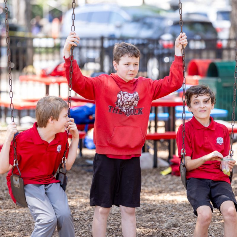 Three students at The Rock School hang out together on the swings during their outside free period.