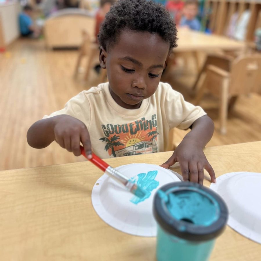 A preschool student paints the back of a plate with a light blue.