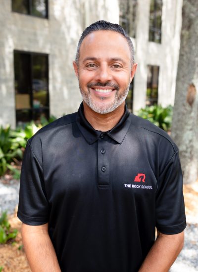Man in The Rock School polo shirt smiling outdoors.