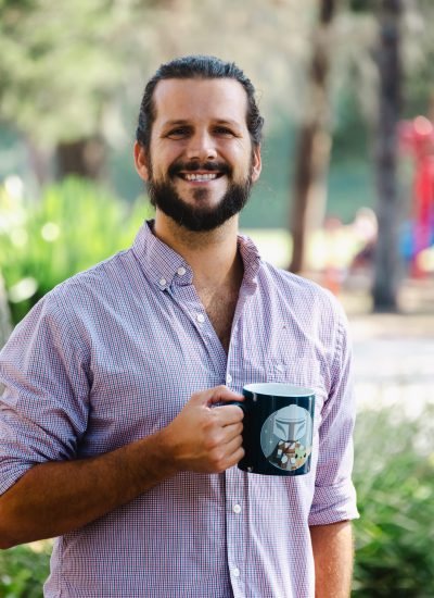 Brandon Bowlin smiles, holding a Grogu mug. Outdoor portrait.