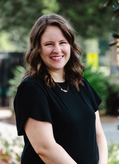 Kayla Pollard smiling outdoors, wearing a black top and gold necklace.