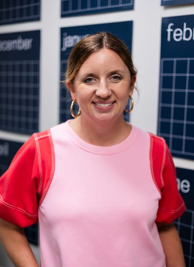 Lacy Basford portrait wearing a pink and red top, smiling at the camera.